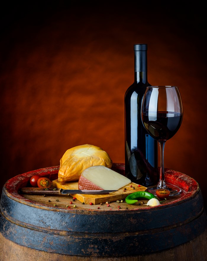 Wine bottle and glass with cheese and vegetables on a barrel