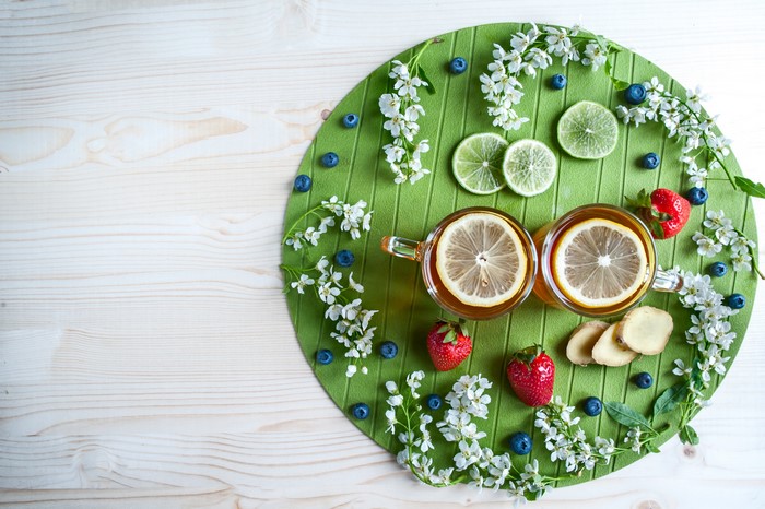 Tea with lemon, strawberries, blueberries, and ginger on a green mat