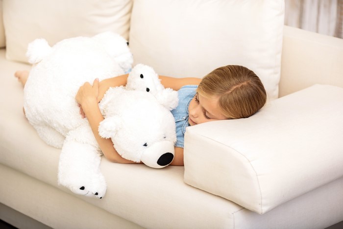 Little girl sleeping with teddy bear on sofa
