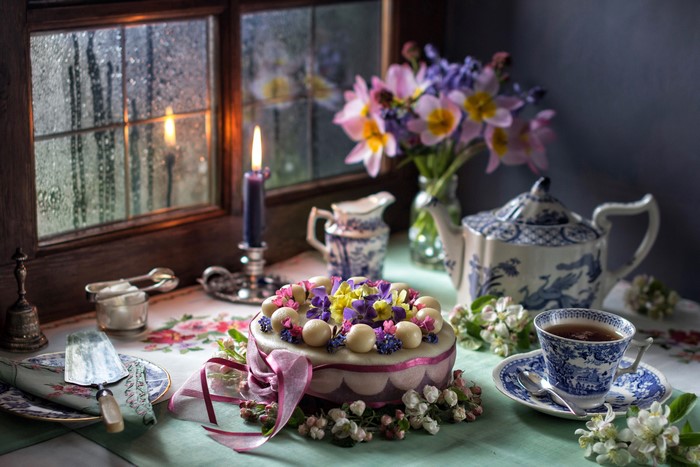 Still-life of a cake, tea set, and flowers by a window
