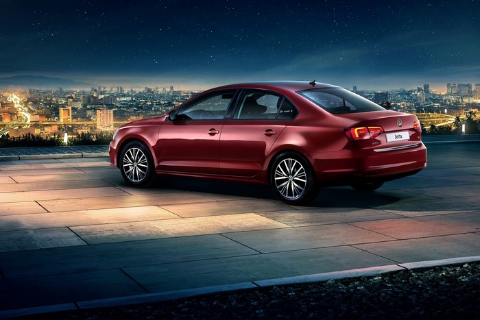 Red Volkswagen Jetta parked at night with city skyline