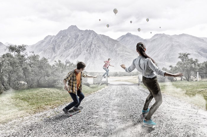 Three people skateboarding with mountains and hot air balloons