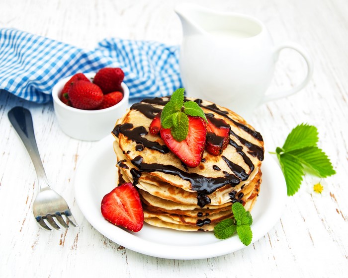 Pancakes with chocolate, strawberries, and mint on a plate with a fork