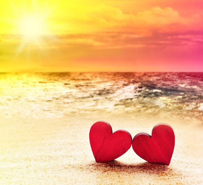 Two red hearts on a beach at sunset