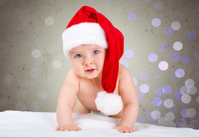 Baby in Santa hat crawling on white blanket