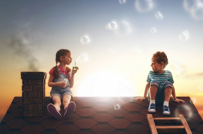Two children blowing soap bubbles on a roof at sunset