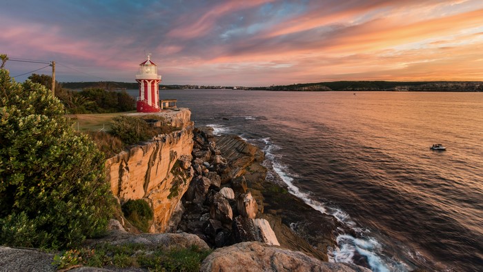 Red and white lighthouse on a cliff at sunset