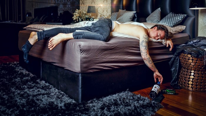 Man sleeping on bed with bottles on floor