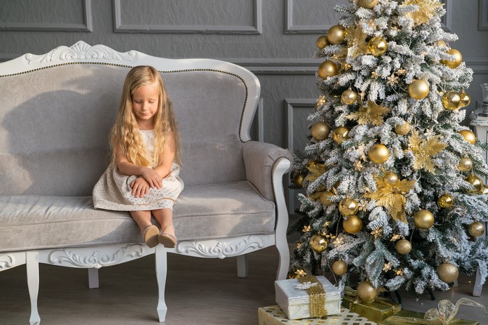 Little girl sitting on a sofa near a Christmas tree