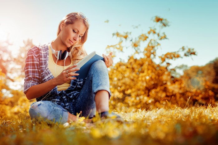 Woman reading a book with headphones in autumn