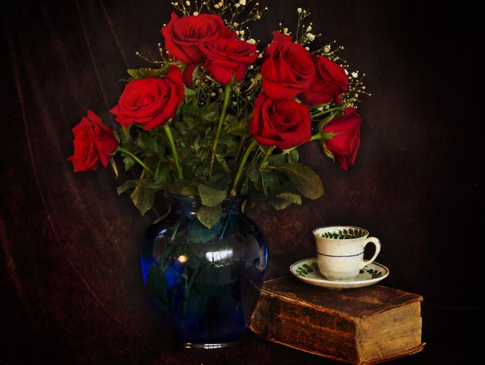 Still-life of red roses in a blue vase with a cup and saucer on a book