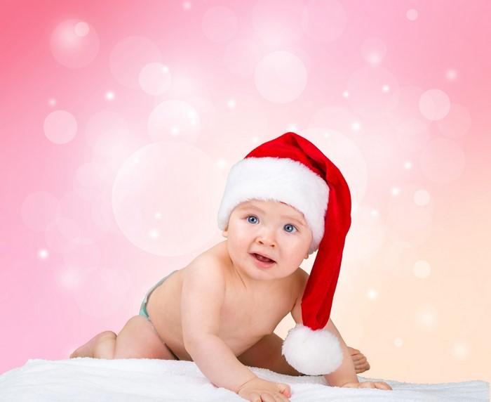 Baby in Santa hat crawling on white blanket