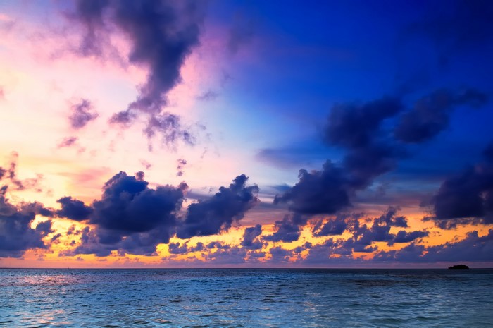 Sunset over the ocean with colorful clouds and a small island