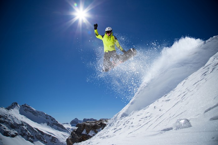 Snowboarder jumping in the air with sun and mountains