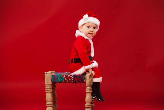 Baby in Santa Claus costume sitting on a stool