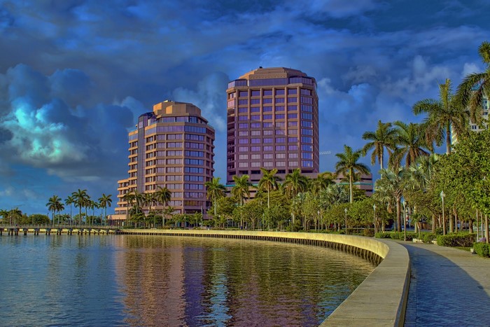 Two modern buildings on a waterfront with palm trees