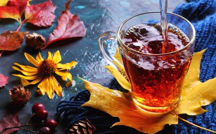 Hot tea being poured into a glass cup with autumn leaves