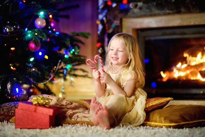Girl with candy canes by Christmas tree and fireplace