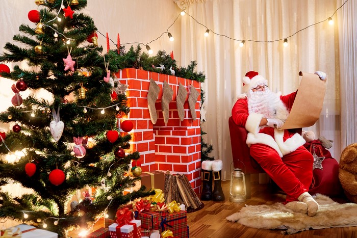 Santa Claus reading a list by a Christmas tree