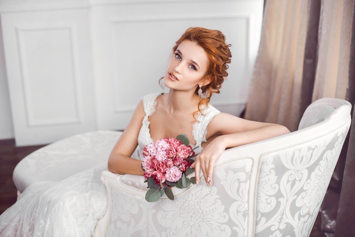 Bride with Red Hair and Pink Bouquet Sitting on Sofa