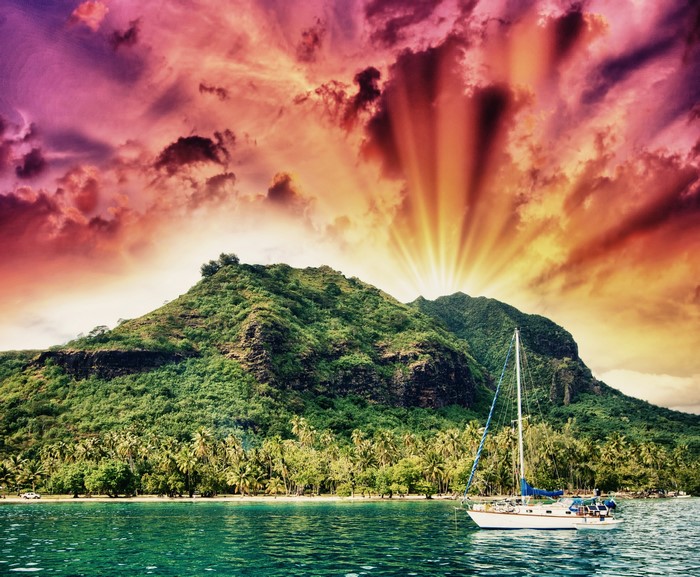 Sailboat near a tropical island with mountains and dramatic sky