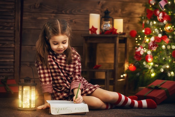 Girl writing a letter to Santa Claus by a Christmas tree