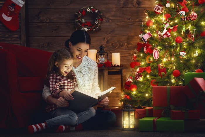 Mother and Daughter Reading a Book by Christmas Tree