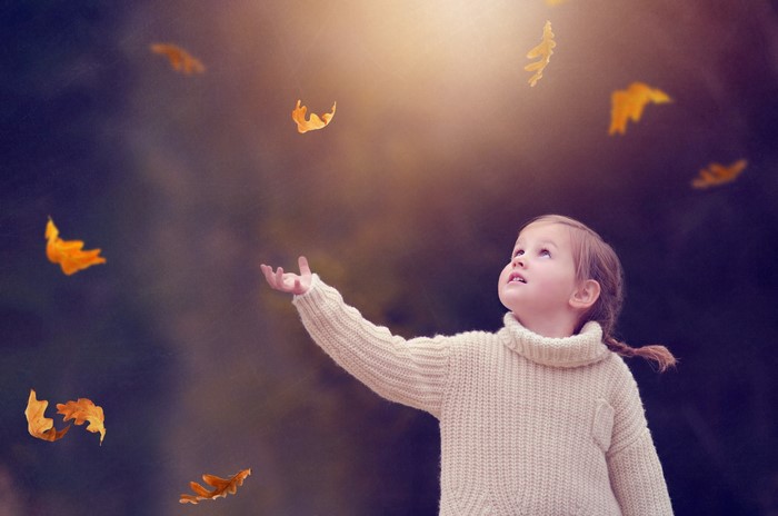 Girl in sweater catching autumn leaves