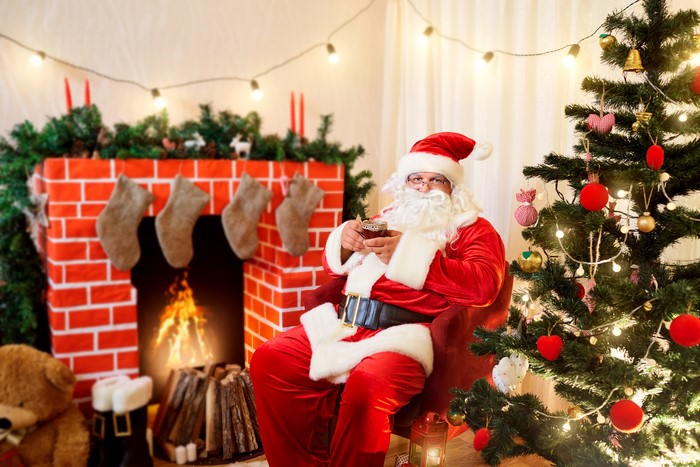 Santa Claus sitting by a fireplace and Christmas tree