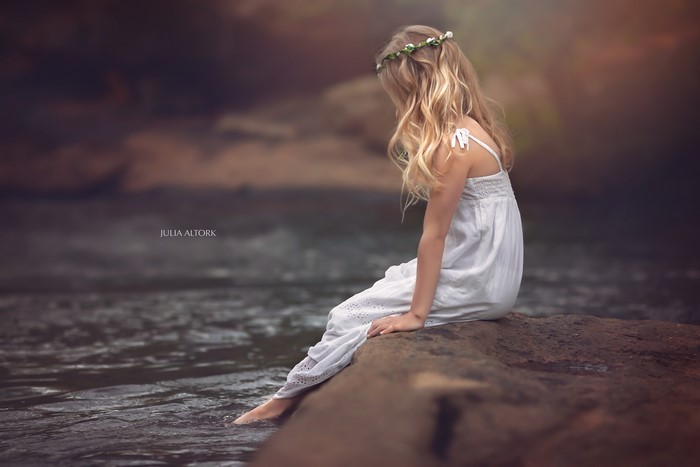 4K Blonde girl sitting by a river