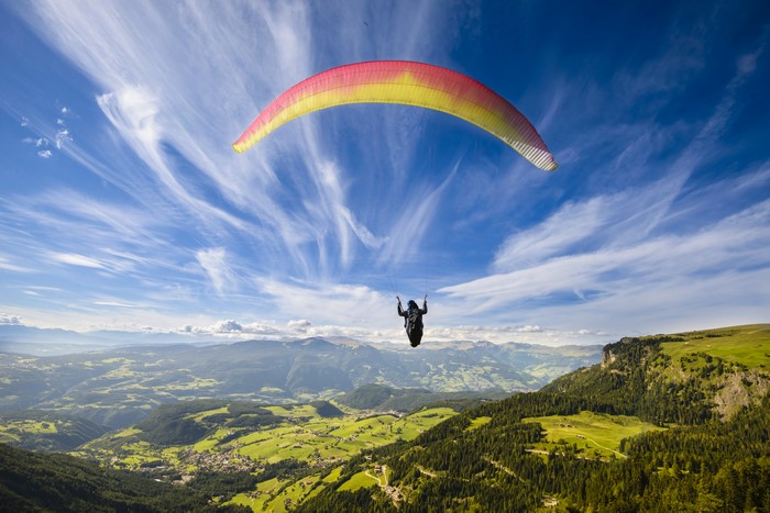 Paragliding over a green valley with mountains