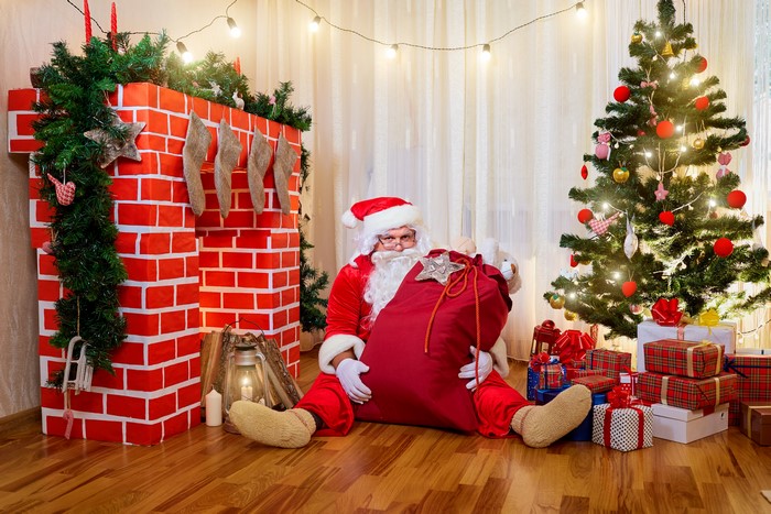 Santa Claus with a gift bag by a fireplace and Christmas tree