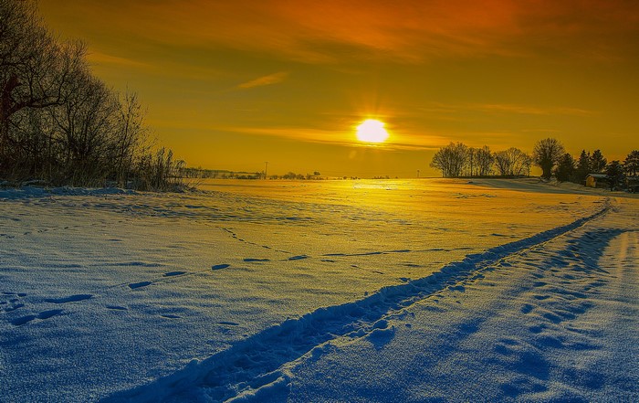 Winter sunset over a snowy field with footprints