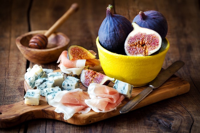 Cheese and figs on a wooden board with honey dipper
