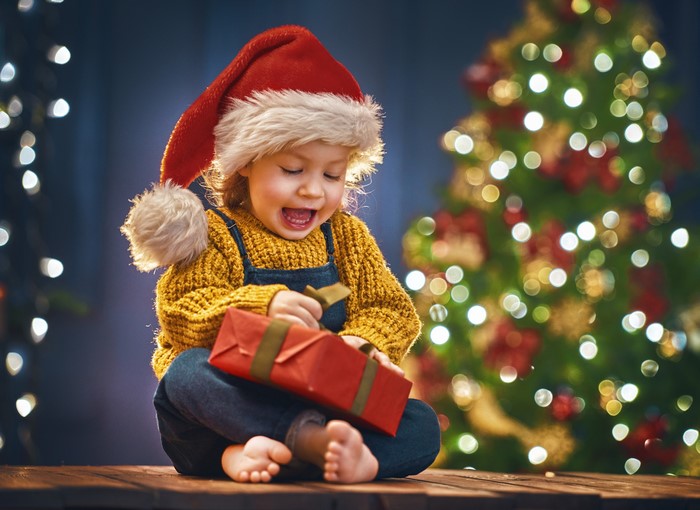 Child in Santa hat opening Christmas gift
