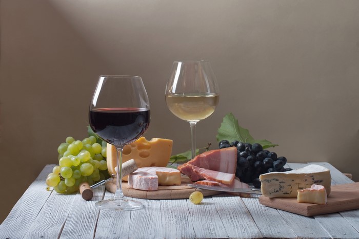 Still life with red and white wine, cheese, grapes, and ham