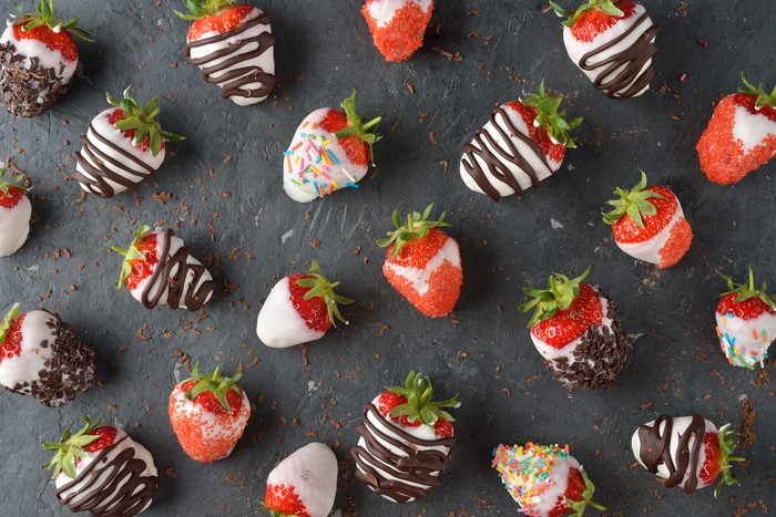 Chocolate-dipped strawberries with toppings on gray background