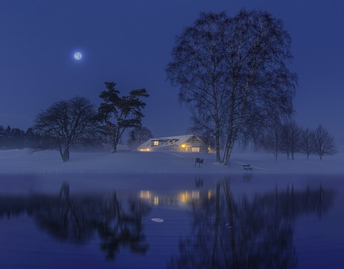 Winter night scene with moonlit house and lake reflection