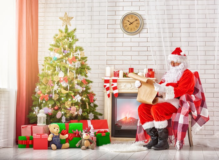 Santa Claus reading a scroll by a Christmas tree