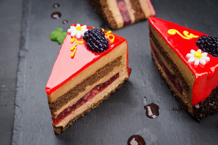 Slices of layered cake with red glaze and blackberry