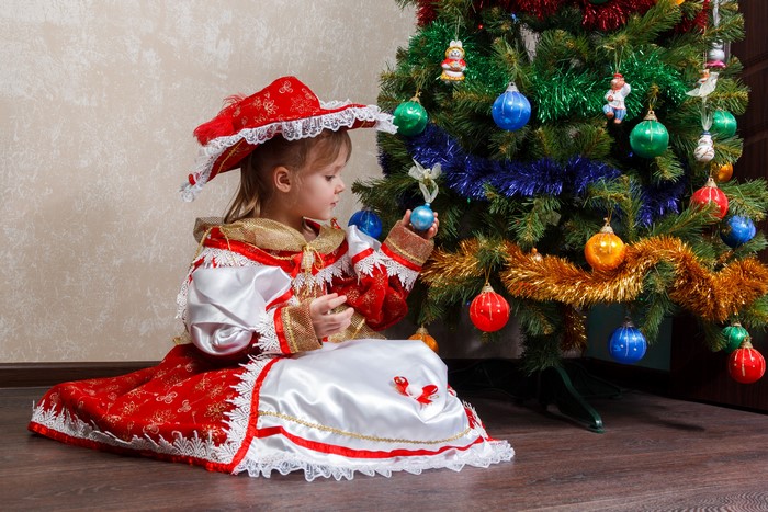 Little girl in costume decorating Christmas tree