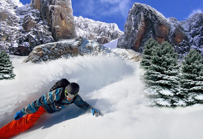 Man snowboarding down a snowy mountain with trees and rocks
