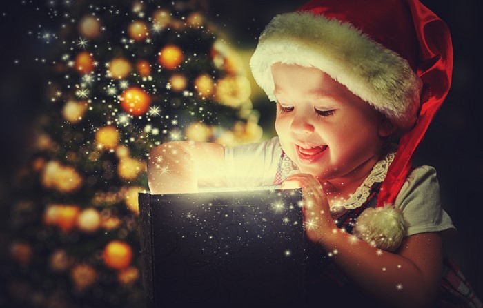 Little girl in Santa hat opening a glowing Christmas gift