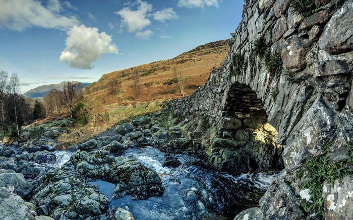 Stone bridge over a rocky stream with hills in background