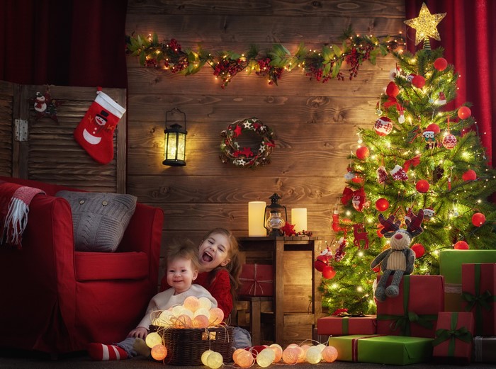 Two young girls by a Christmas tree with gifts