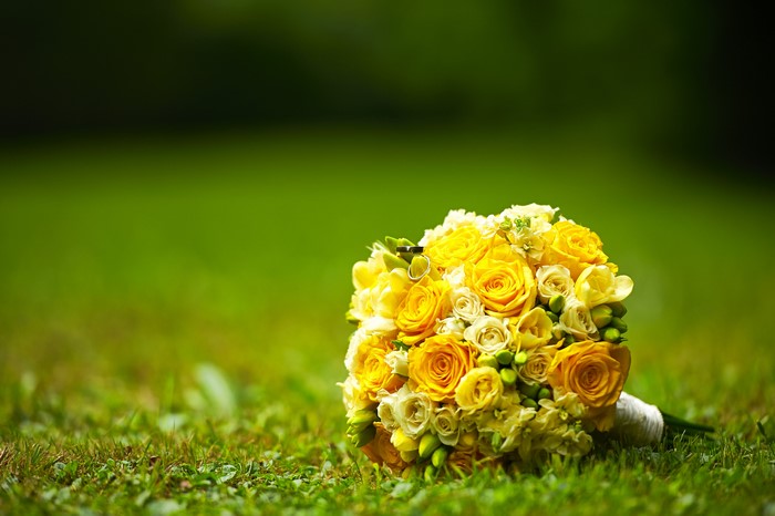 Yellow rose bouquet with wedding rings on grass