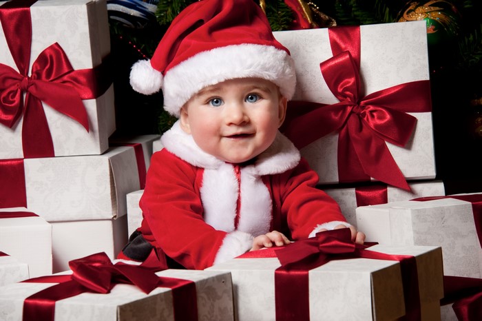 Baby in Santa costume surrounded by Christmas gifts
