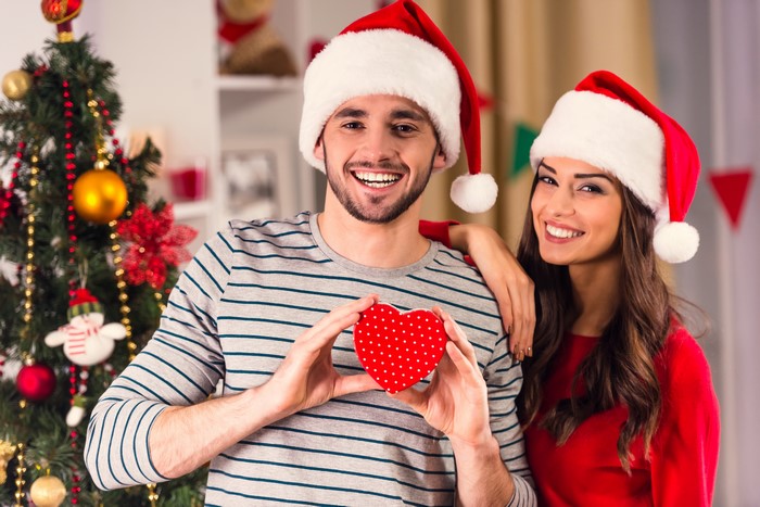 Couple in Santa Hats with Heart Gift by Christmas Tree