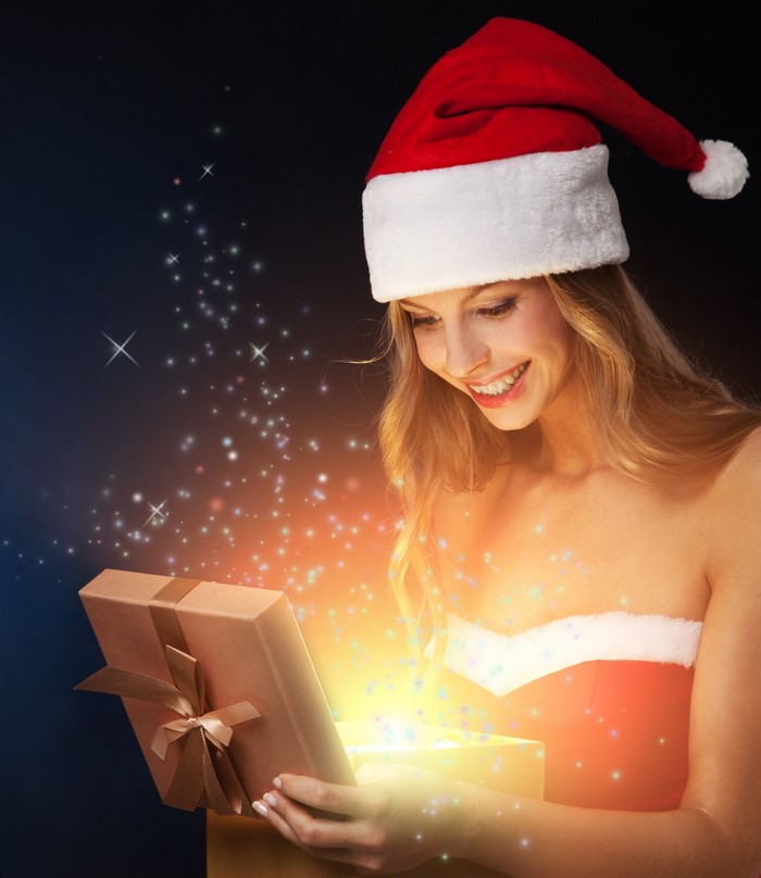 Woman in Santa hat opening a glowing Christmas gift