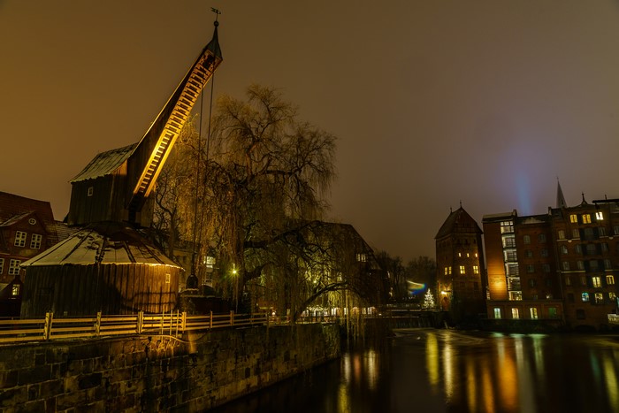 Crane and buildings by river at night in Luneburg, Germany